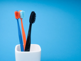 Three toothbrushes, black, blue and orange, for oral care, in a white toothbrush holder on a blue background
