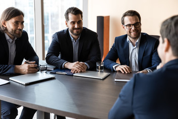 Applicant sitting in front three happy HR businessmen speaking.