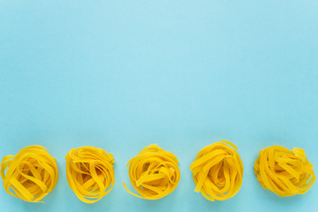 Unprepared wheat pasta in the form of a nest on a blue background with copying space
