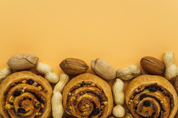 Cinnamon rolls, raisins and nuts. Pecans and peanuts on orange background with copy space