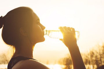 Young beautiful woman drinks water from a bottle in the sun