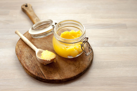 Ghee clarified butter desi in glass jar with spoon made from wood on natural wooden background