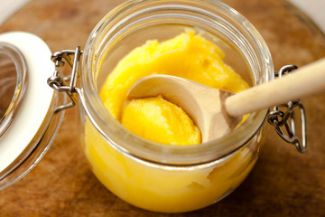 Ghee clarified butter desi in glass jar with spoon made from wood on natural wooden background