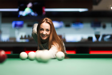 Pretty girl getting ready to hit a ball in a billiard table
