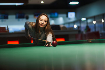 Girl plays billiards in the club.