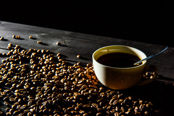 a cup of coffee stands on a black wooden table, coffee beans are scattered around.