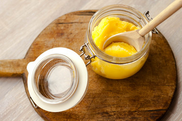 Ghee clarified butter desi in glass jar with spoon made from wood on natural wooden background