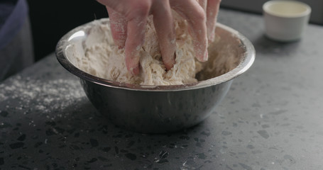 man mixing dough in steel bowl on concrete countertop