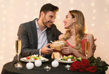 Obraz na płótnie Canvas Affectionate Man Surprising Girlfriend With Gift At Romantic Restaurant Dinner