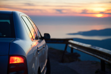 Fototapeta na wymiar Road trip by car at sunset. Parking on roadside of narrow mountain way. Stop for rest with red headlamp. View of amazing sea coastline. Concept of outdoor adventure, summer vacation. Copy space