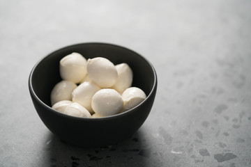 Small mozzarella balls in black bowl on concrete background