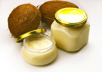 Solid homemade coconut oil in glass jar with metal gold lid and fresh coconuts on a white background
