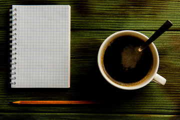 pencil padand and a cup of coffee on a green wooden table.