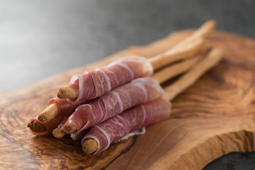 Grissini with prosciutto on olive wood board