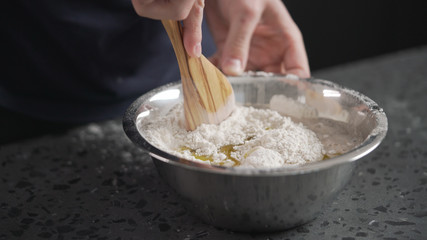man mixing wet ingredients into flour in steel bowl on concrete countertop