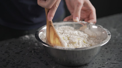 man mixing wet ingredients into flour in steel bowl on concrete countertop