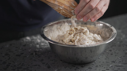 man mixing dough in steel bowl on concrete countertop