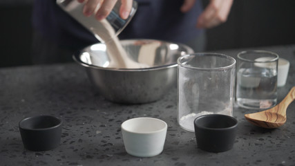 man adds dry ingredients into flour in steel bowl on concrete countertop