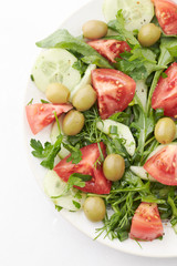 Salad with green Olives, Tomatoes, Cucumber and Rocket on bright Background. Healthy Snack Idea. Close up.