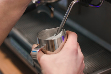 Hand with a pitcher. Whipping milk. Barista