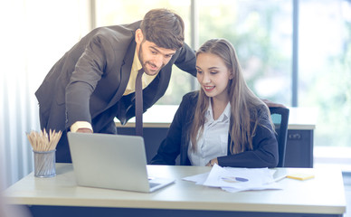 A young business man wearing a suit standing to teach working with a female secretary in the office Business concepts and team work