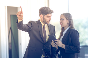 The young man in a suit is standing talking to a female secretary in the office. The concept of business and teamwork