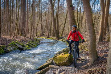 nice active senior woman riding her electric mountain bike in early spring along a little river...