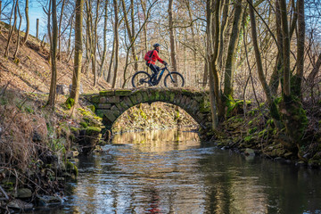 nice active senior woman riding her electric mountain bike in early spring along a little river...