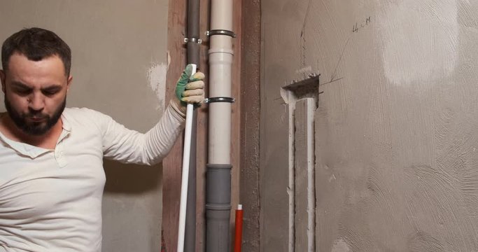 Bearded plumber cuts plastic pipes with special cutter, paves new sewer in apartment, repairs, blows off plastic shavings, construction worker, repairing leaks, updating, replacing, bathroom, sewage