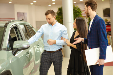 Naklejka premium young couple, man and woman choosing new auto in representative dealership, consulting with salesman. side view