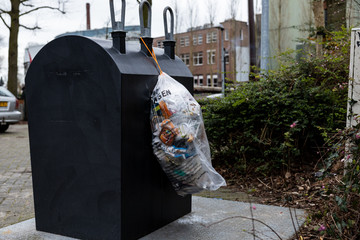 Gouda, South Holland/The Netherlands - February 15 2020: Plastic waste bag hanging on a container for collecting trash being left there by one of the cities inhabitants