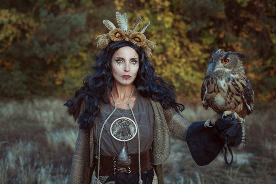 Portrait of a shaman woman in the forest. She has an eagle owl in her hand.