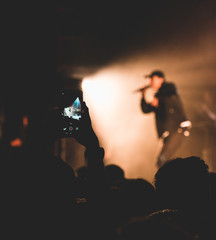 Public prenant en photo au téléphone un artiste sur scène lors d'un concert de rap français