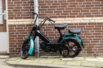 Obraz na płótnie Canvas Black and green moped left behind with a lock on the rear wheel and also a flat tire in front of a brick wall
