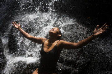 Fototapeta premium young attractive and blissful Asian Indonesian woman overwhelmed by the beauty of natural waterfall in tropical jungle enjoying happy the amazing and exotic travel destination