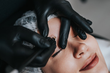 Eyebrows microblading concept. Cosmetologist preparing young woman for eyebrow permanent makeup...