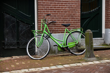 Fototapeta na wymiar Gouda, South Holland/The Netherlands - February 15 2020: bright green locked bike in front of a brick wall and doors of a building behind it and the bikes has a flat front tire