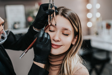 Cosmetologist measures the proportions of the eyebrows with the ruler. Micropigmentation work flow in a beauty salon.