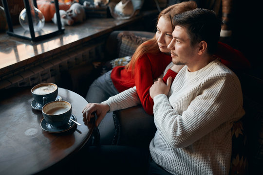 Thoughtful Pensive Couple Looking At The Window, While Sitting At The Wooden Table. Close Up Side View Photo. Copy Space