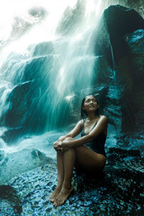 young attractive and blissful Asian Indonesian woman overwhelmed by the beauty of natural waterfall in tropical jungle enjoying happy the amazing and exotic travel destination