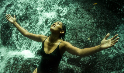 Fototapeta premium young attractive and blissful Asian Indonesian woman overwhelmed by the beauty of natural waterfall in tropical jungle enjoying happy the amazing and exotic travel destination