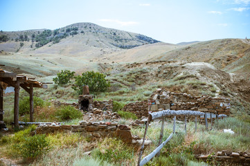 Fototapeta na wymiar Old ruined log house and stone stove in the yard in Crimean steppe on a background of mountains