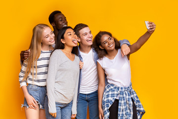 Cheerful group of multiethnic friends taking selfie over yellow background