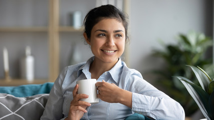 Happy indian woman drink warm tea relaxing at home