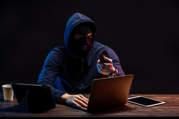 hacker male use laptop to gain unauthorized access to data, isolated in dark space. person in pullover with high knowledge of specific technology field, intervenes premeditatedly in different systems