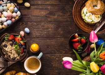Rustic easter breakfast flat lay with eggs bagels, tulips, croissants, egg, oatmeal with berries, colored quail eggs and spring holidays decorations. Top view, copy space.