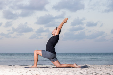 Young yoga man wearing black t-shirt at the beach, relaxing, breathing and meditating in a natural environment with palm trees and ocean as background.  - obrazy, fototapety, plakaty