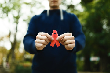 red aids ribbon in hand on green background, HIV - obrazy, fototapety, plakaty