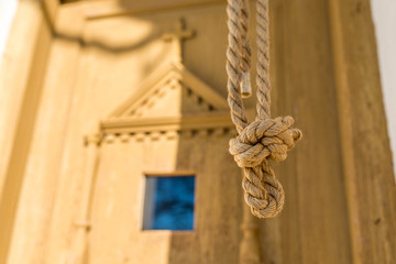 Hemp rope for ringing the bell in front of a carved wooden door on catholic chapel.