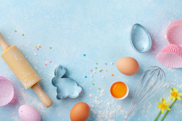 Easter baking background with rolling pin, whisk, eggs, flour and colorful confetti on blue table...